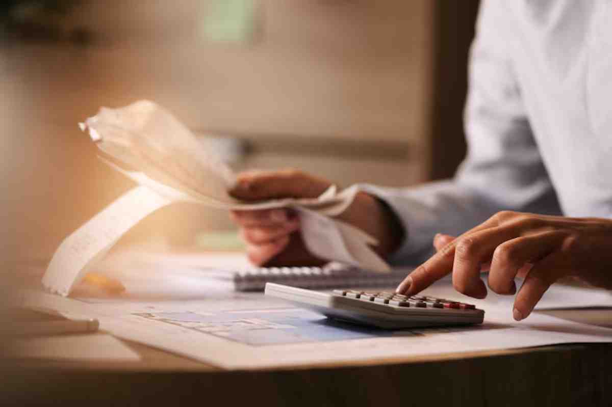 A person sits at a desk, calculating expenses using a calculator while reviewing receipts and financial documents.