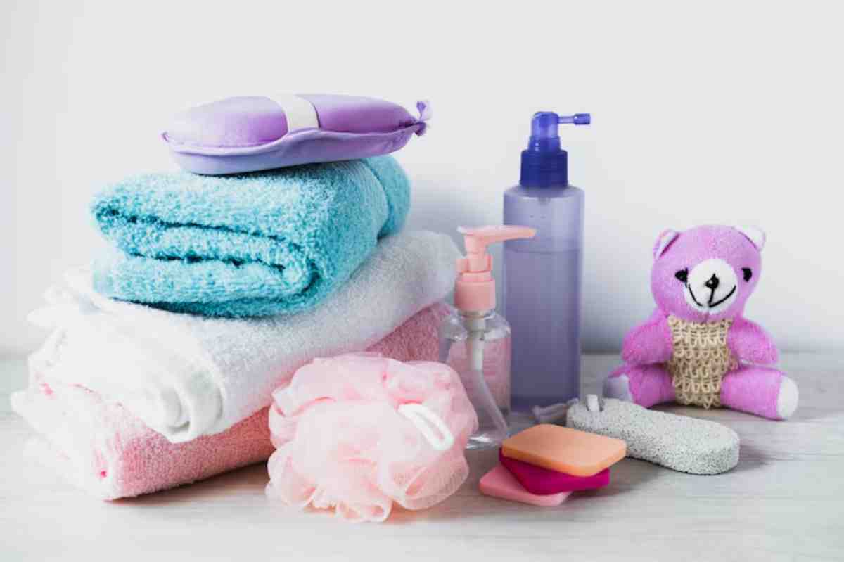 A collection of colorful towels, bath products, a pink teddy bear, and sponges arranged on a white background.