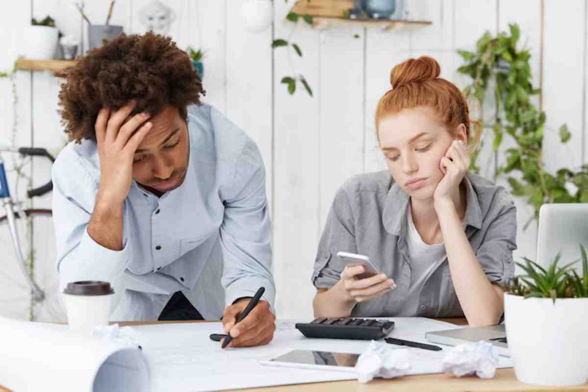 Two colleagues collaborate at a desk cluttered with papers, a laptop, and coffee, deep in thought during a brainstorming session.
