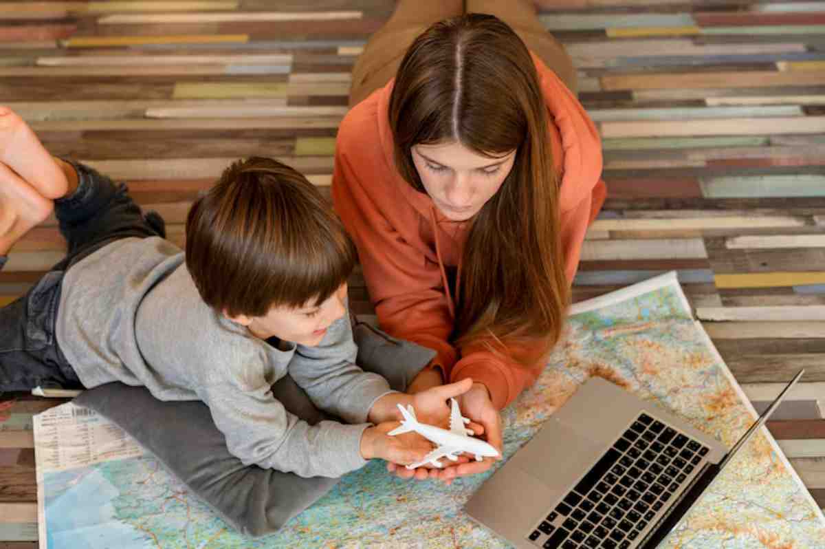 A child and an adult are on a colorful floor, examining a map and a white toy airplane, with a laptop nearby.