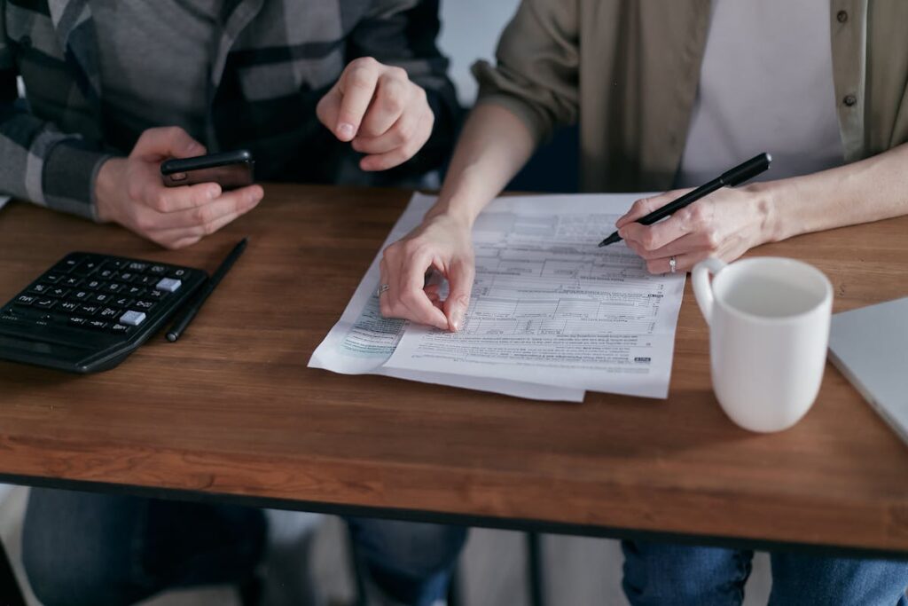 Two people discussing paperwork at a table, one holds a smartphone while the other points at the document, a calculator nearby.