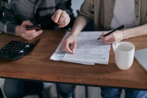 Two people discussing paperwork at a table, one holds a smartphone while the other points at the document, a calculator nearby.