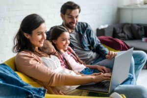 A family relaxes on a yellow couch, engaged with a laptop, showcasing bonding and collaborative activity in a cozy living room.