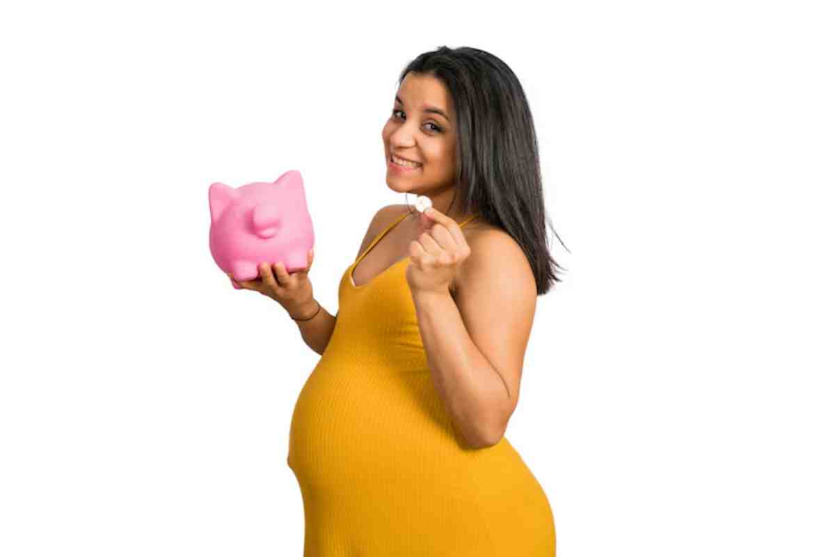 A pregnant woman in a yellow dress holds a pink piggy bank in one hand and a coin in the other, smiling confidently.