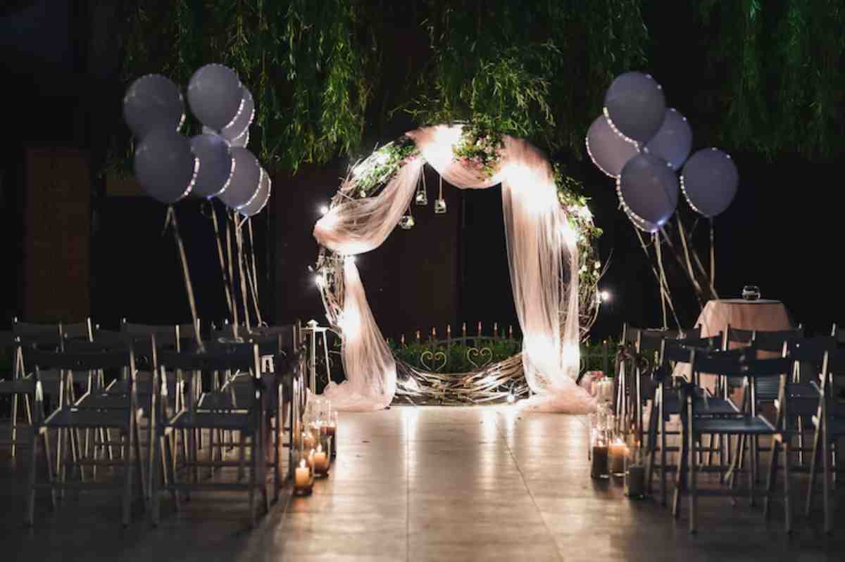 A beautifully decorated wedding altar with draped fabric, fairy lights, and candles, surrounded by chairs and purple balloons.
