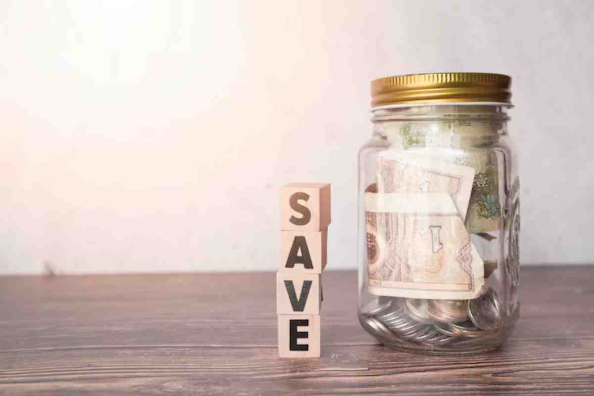 A glass jar filled with cash and coins sits next to wooden blocks spelling save,symbolizing savings and financial planning.