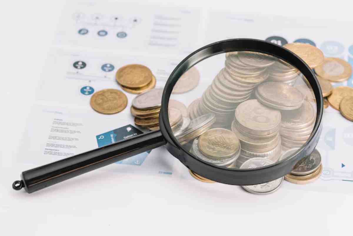 A magnifying glass focuses on a pile of coins resting on documents, symbolizing financial analysis or research.
