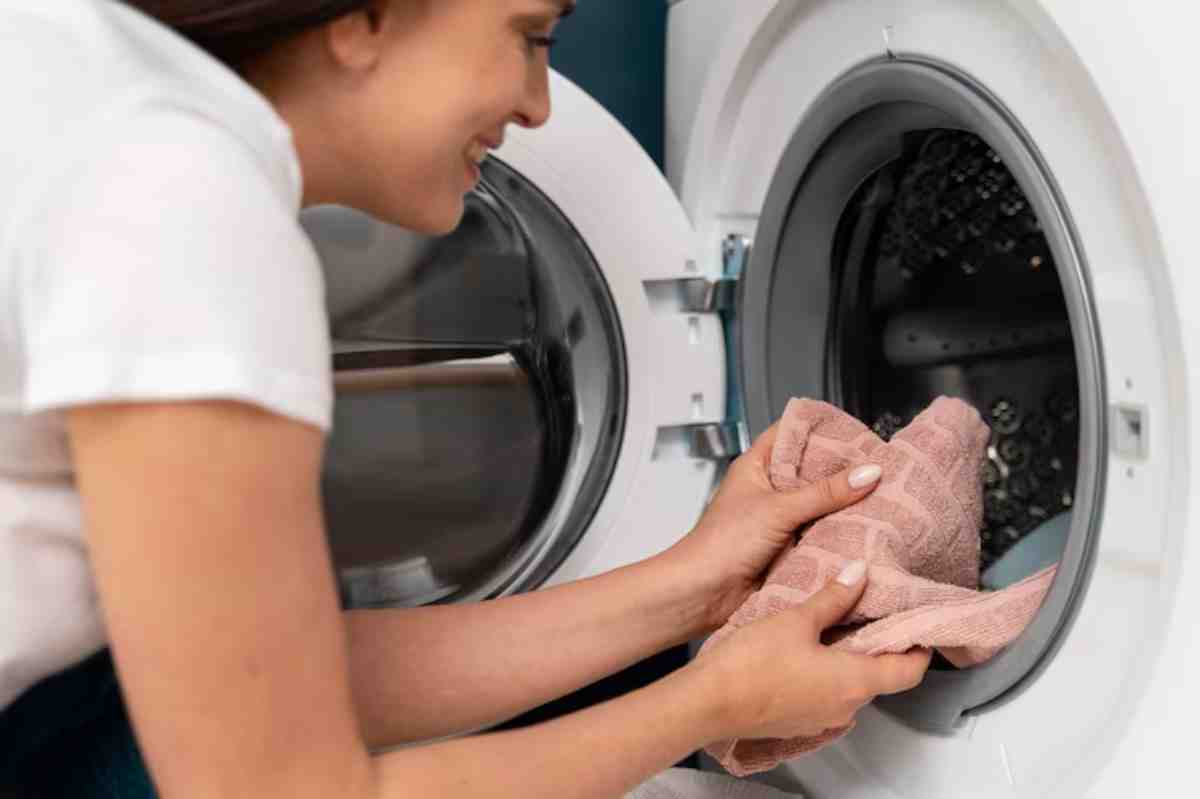 A person is loading a pink towel into a front-loading washing machine, ready to start a laundry cycle.