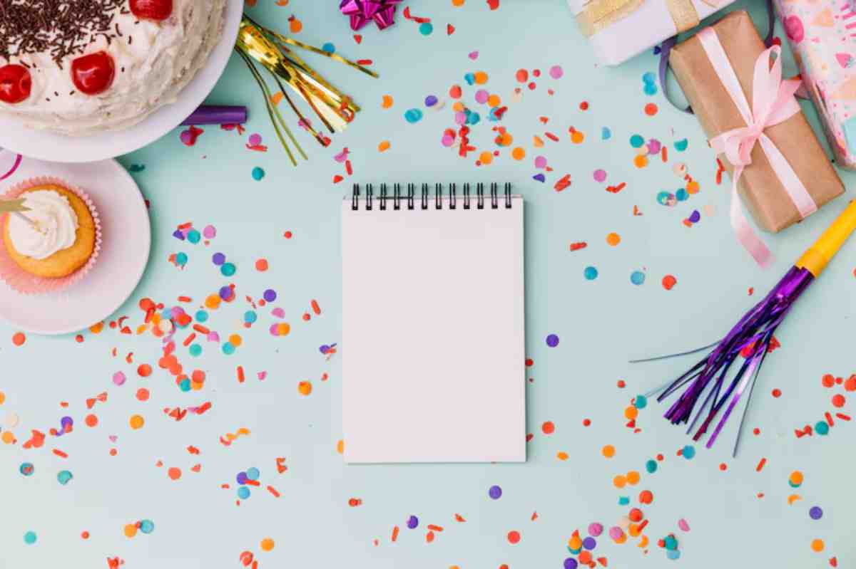 A festive table setting with a cake, cupcake, colorful confetti, gifts, and a blank notepad, perfect for a celebration.