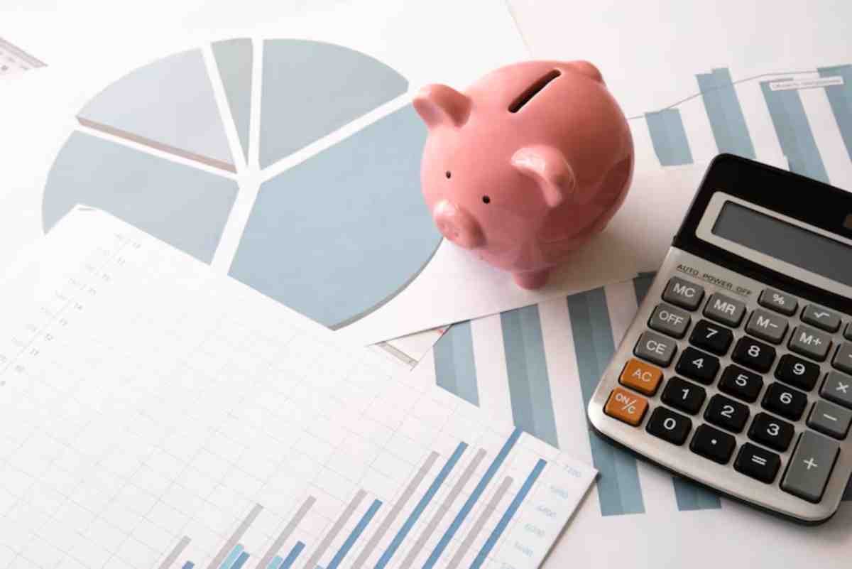 A pink piggy bank sits on financial reports and charts alongside a calculator, symbolizing budgeting and savings.