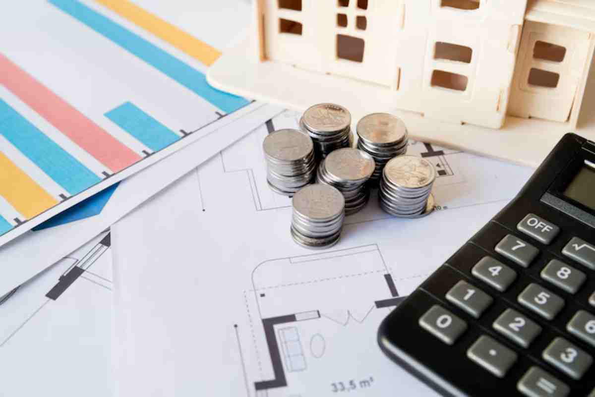 A stack of coins beside a calculator, on top of architectural blueprints and colorful charts, representing financial planning.