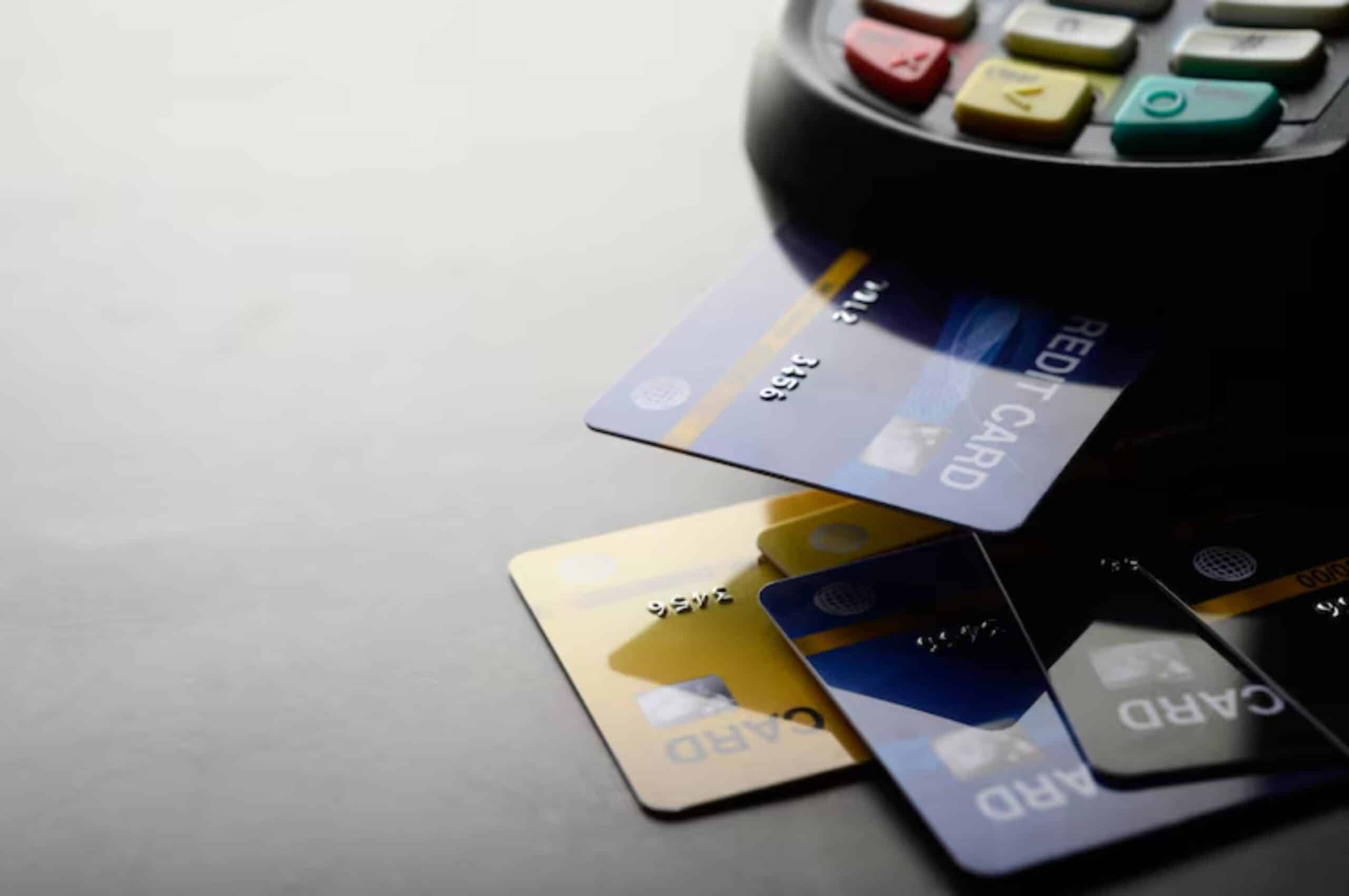 A close-up of credit cards in blue and gold resting beside a card reader with colorful buttons on a dark surface.