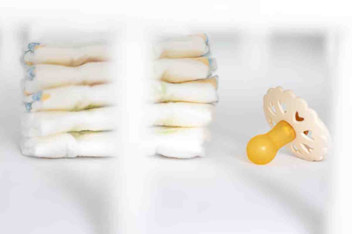 A stack of baby diapers next to a yellow pacifier on a white surface, showcasing essential items for infant care.