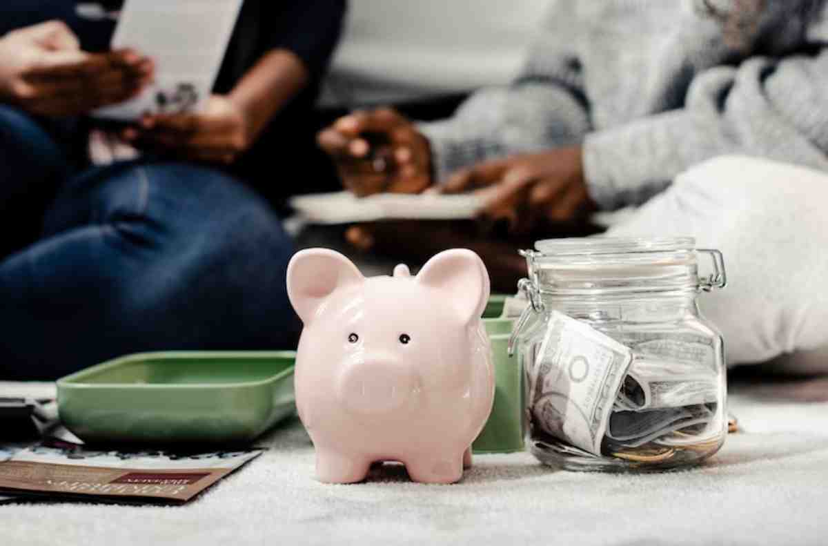 A pink piggy bank sits beside a glass jar filled with cash, while hands hold financial documents, indicating a budgeting session.
