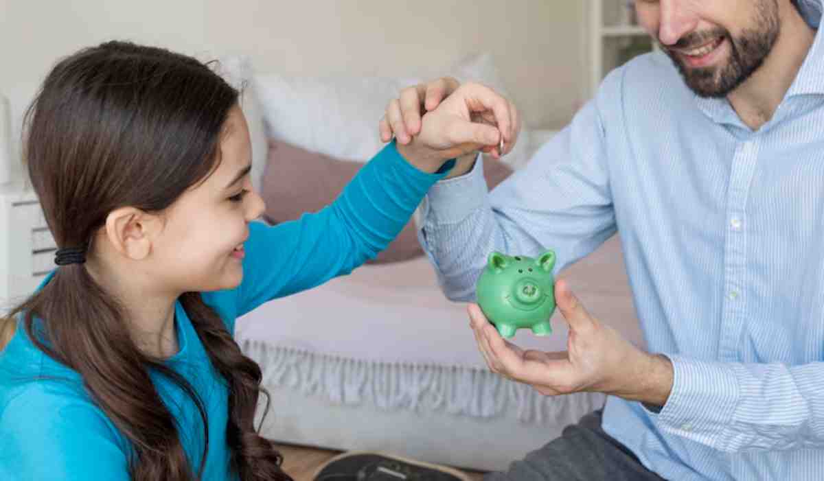 A child reaching out for a green piggy bank held by an adult, both engaged in a learning moment about saving money.